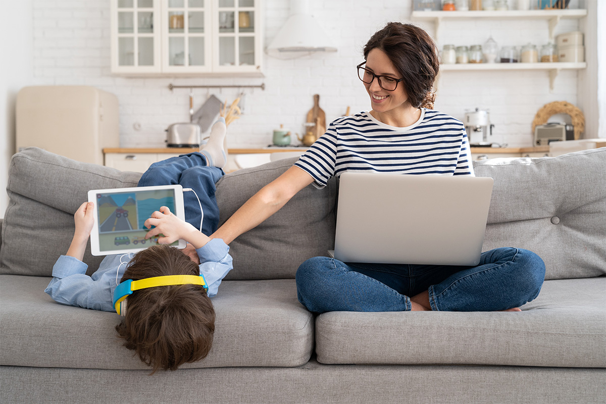 Frau mit Laptop und Kund mit Tablet auf einem Sofa im Wohnzimmer